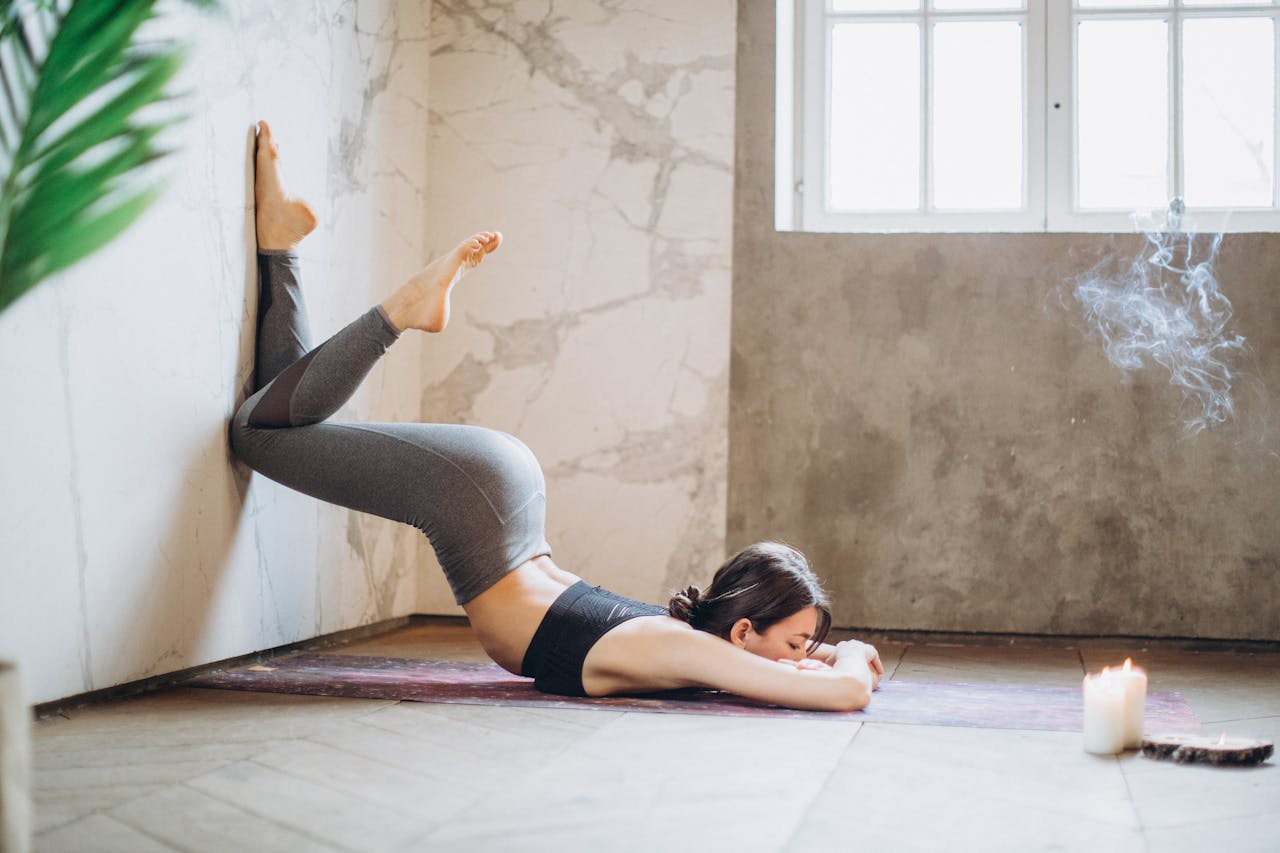 Woman practicing yoga against a wall in a peaceful indoor setting with candles.